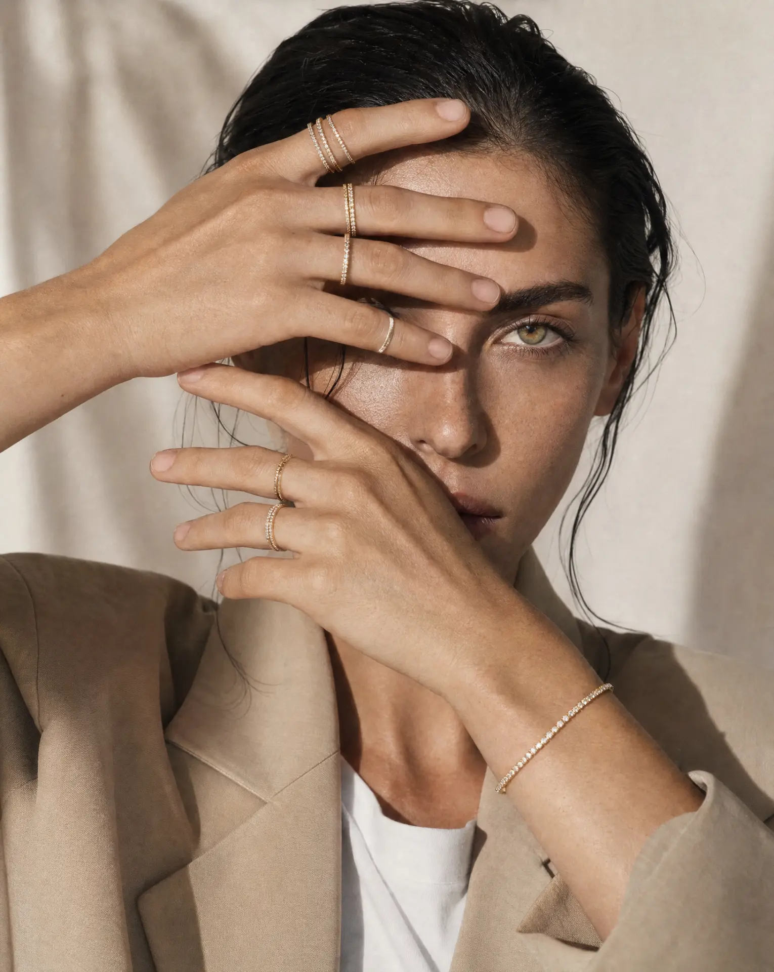 Stacked gold rings and tennis bracelet framing a model's face