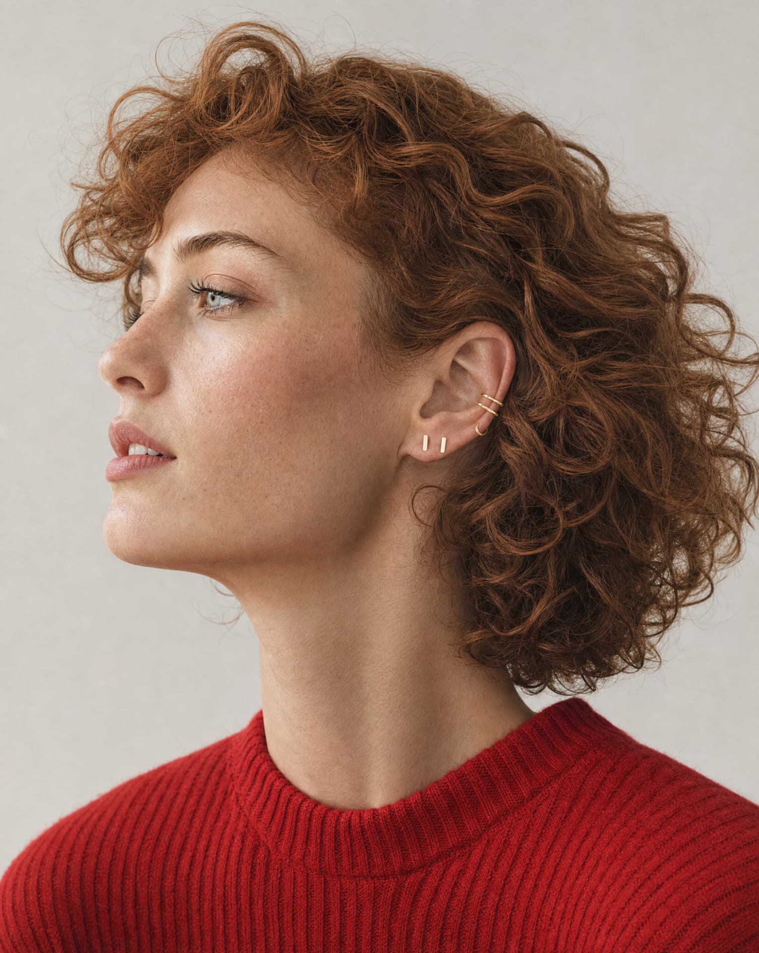 Profile portrait with gold ear cuff and bar studs, red knit sweater